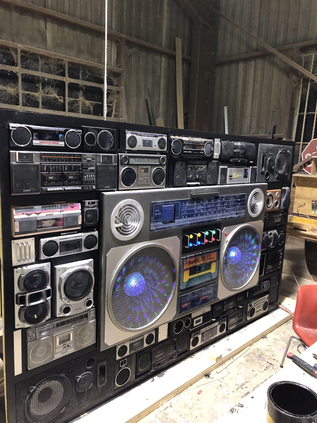 A wall built from vintage boomboxes and speakers, lit from inside
